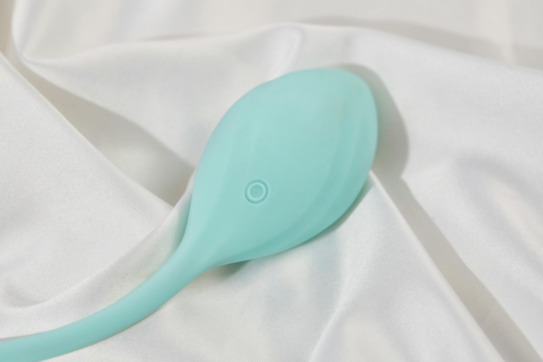 Teal lemon vibrator resting on white silk fabric
