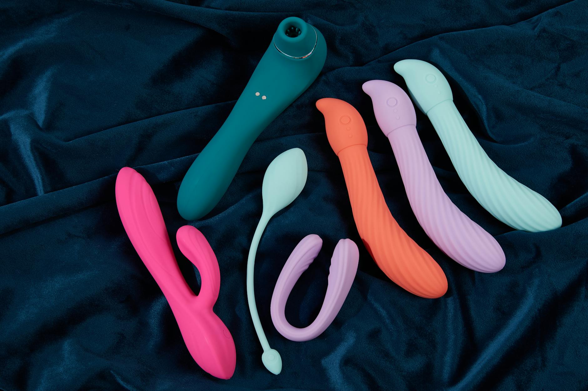 Colorful silicone vibrators and toys displayed on dark blue fabric, showing variety and inclusive design choices.