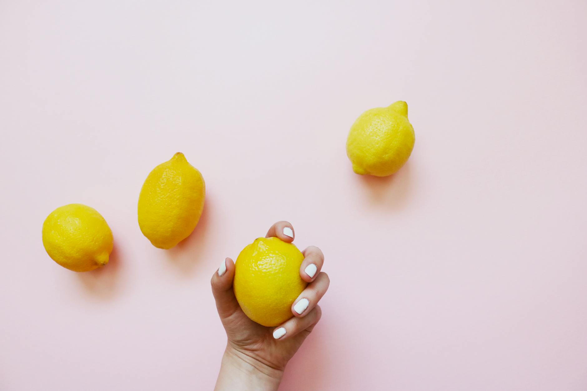 A hand holding a fresh lemon on soft pink background, symbolizing renewed sensation and pleasure