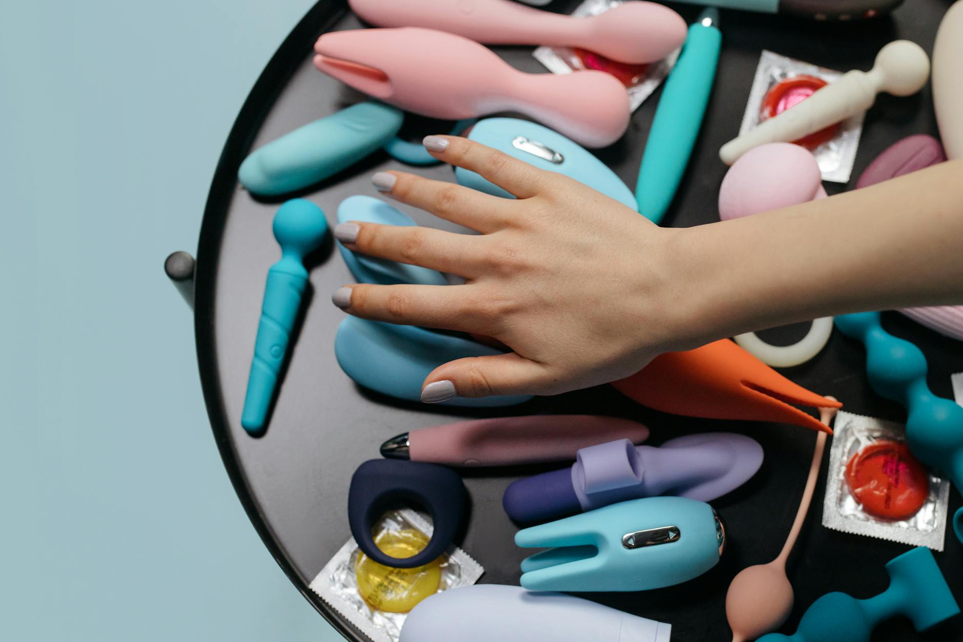 Hand reaching toward colorful sex toys arranged on a table