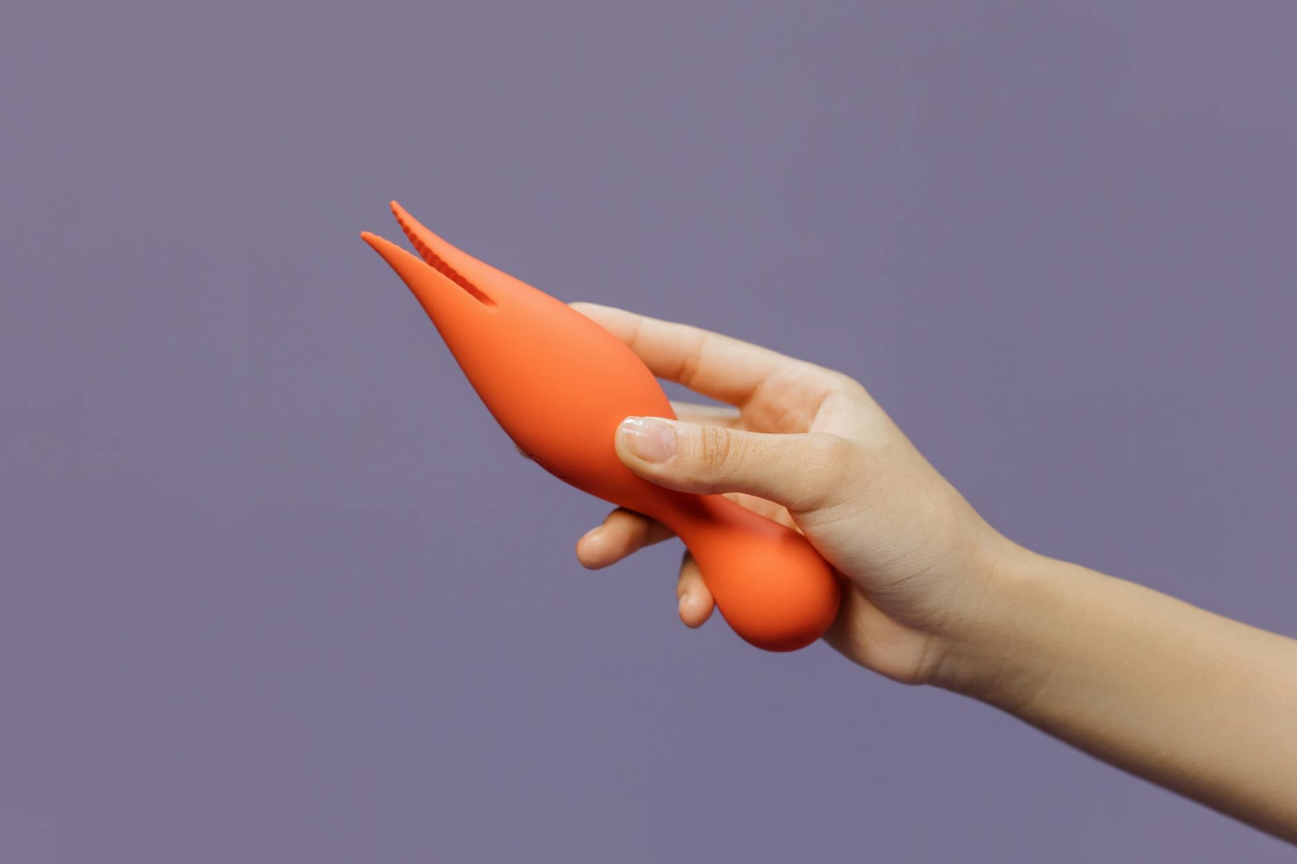 A hand holding a lemon-colored vibrator against a minimalist purple backdrop, highlighting modern design and intimacy.