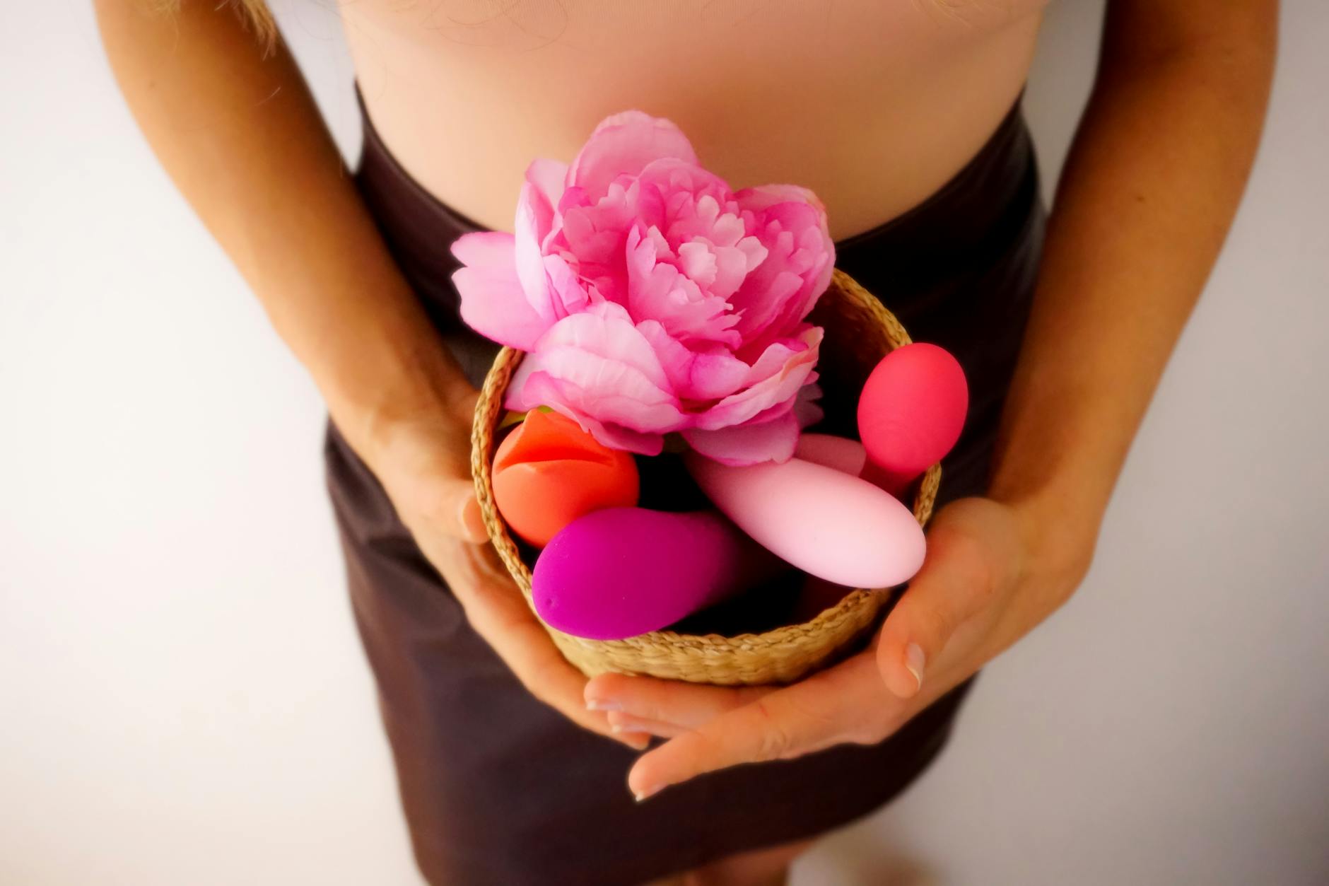 A basket of colorful vibrators and intimate wellness products displayed with natural flowers
